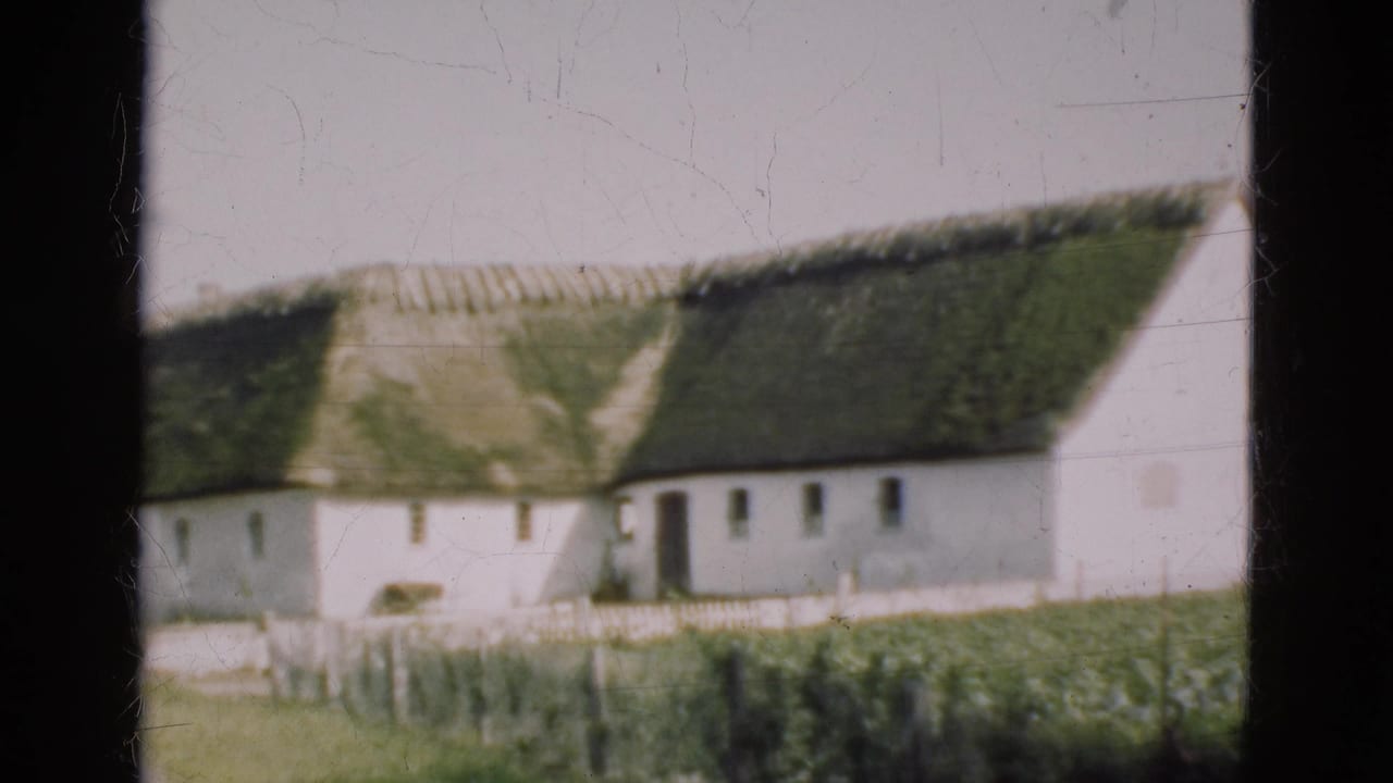 1975 Denmark 8mm view of a white rural cottage with green thatch, fencing, and vegetation seen through dark vertical framing.