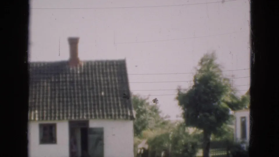 1975 Denmark 8mm view of a small white house with dark tile roof, brick chimney, open doorway, window, and nearby tree.