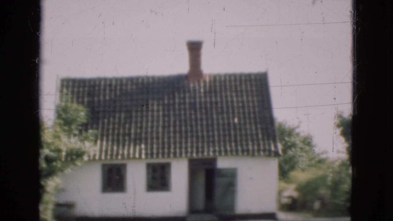 1975 Denmark 8mm view of a white house with tiled roof, chimney, trees, and a dark window frame in the foreground.