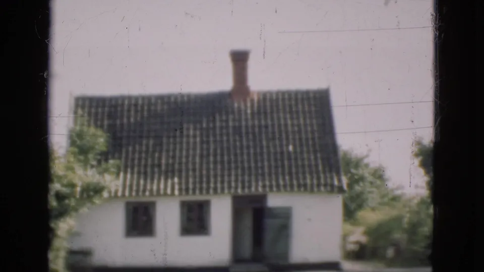 1975 Denmark 8mm view of a white house with tiled roof, chimney, trees, and a dark window frame in the foreground.