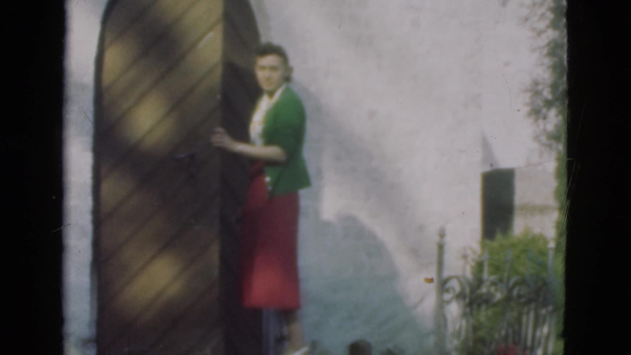 Woman faces the camera while holding or opening the wooden door.