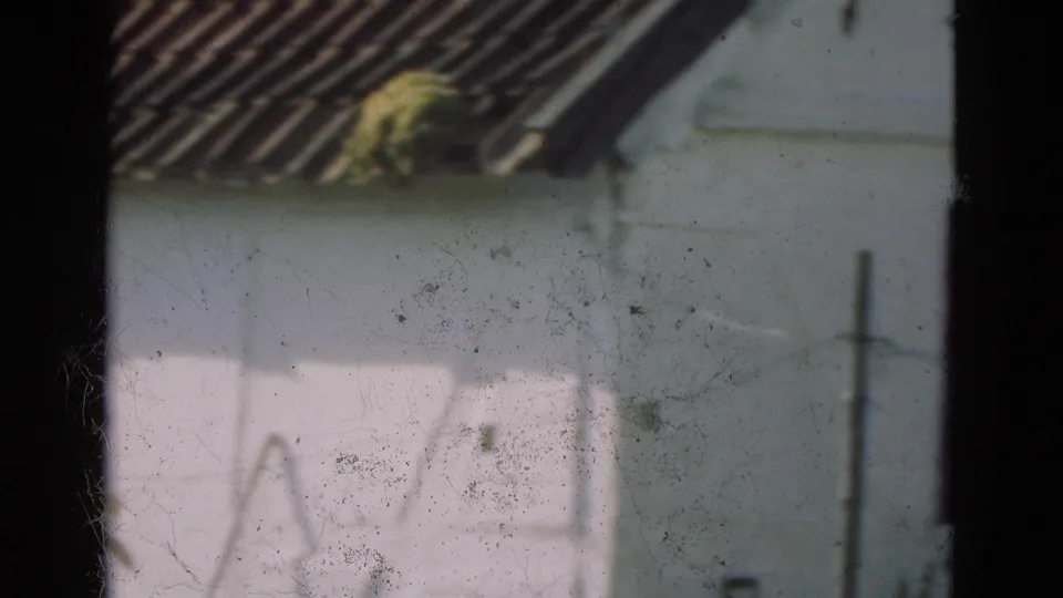 1975 Denmark 8mm frame of a whitewashed rural wall and tiled roof seen through a dark window frame, with visible dust and scratches.