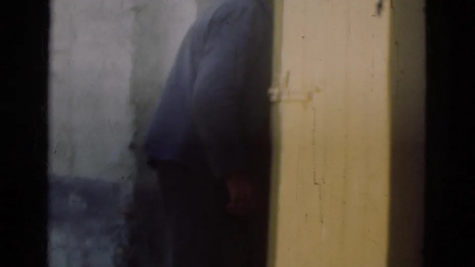1975 Denmark 8mm frame showing a man in dark outerwear beside a yellow door and blue-gray exterior wall.