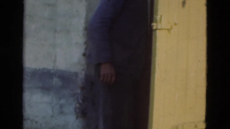 1975 Denmark 8mm frame of a man beside a yellow entrance door, his hand near the doorframe as if closing or handling it.