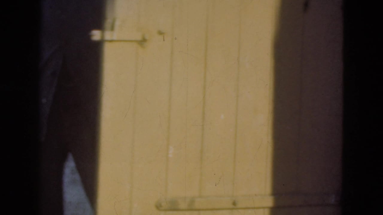 A large plank door with a simple metal latch fills the frame, with a person partly visible in the dark doorway area.