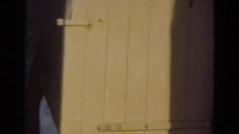 A large plank door with a simple metal latch fills the frame, with a person partly visible in the dark doorway area.