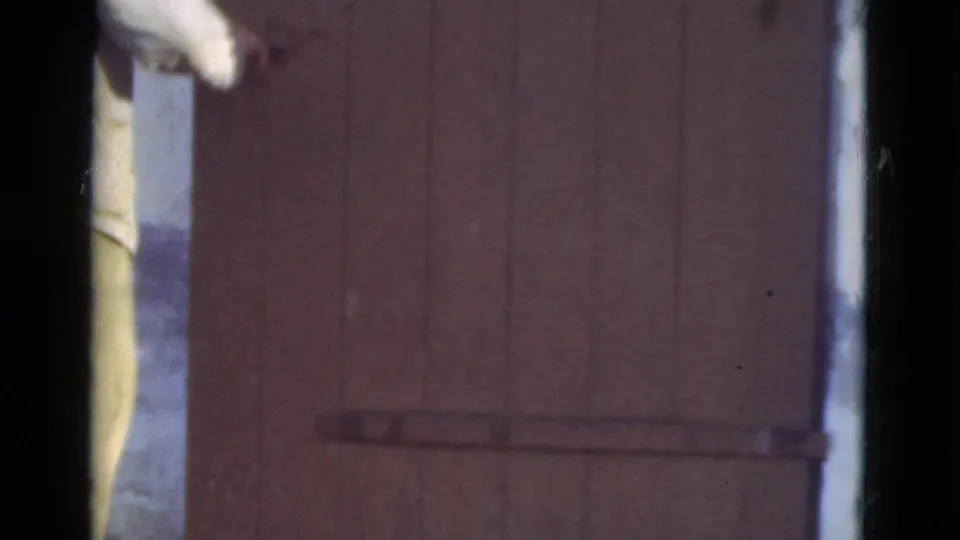 The brown plank door appears nearly closed, with a cropped figure at the left edge and the metal latch visible low on the door.