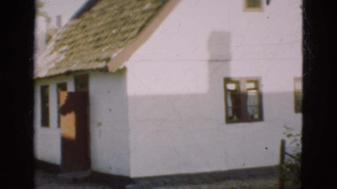 White gable wall with thatched roof, open doorway, windows, and chimney shadow.