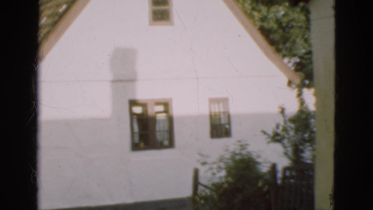 1975 Denmark 8mm frame showing a white country house gable viewed through dark window-like framing, with tiled roof and greenery.