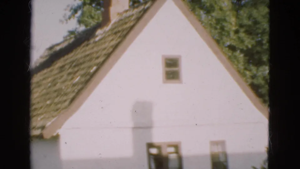 1975 Denmark home-movie frame showing the tiled roof and white gable of a country house, with chimney and small windows.