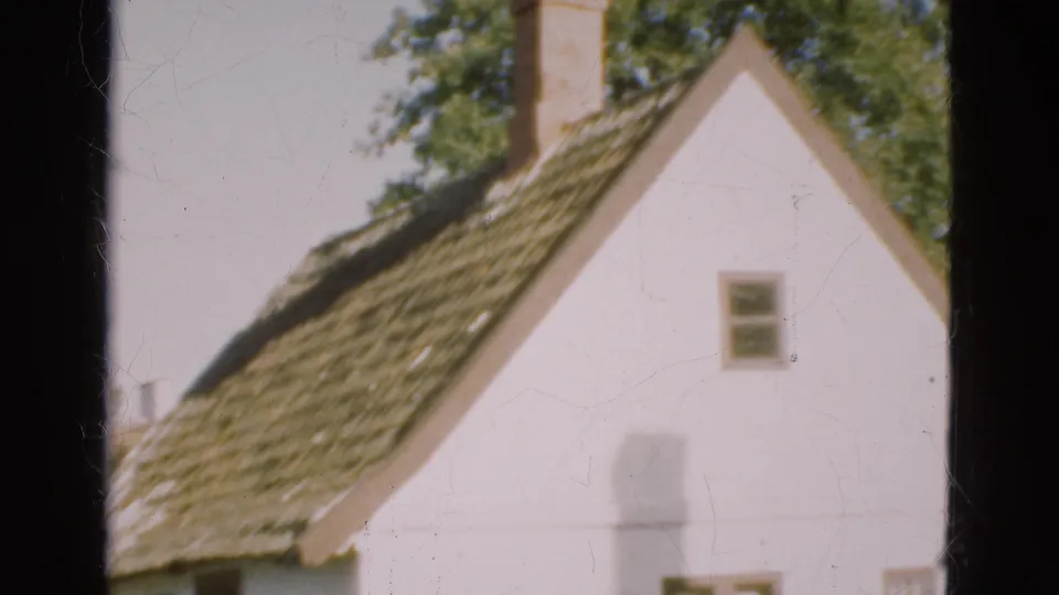 1975 Denmark 8mm frame with an angled view of the house roof and white gable, including chimney, small window and surrounding trees.