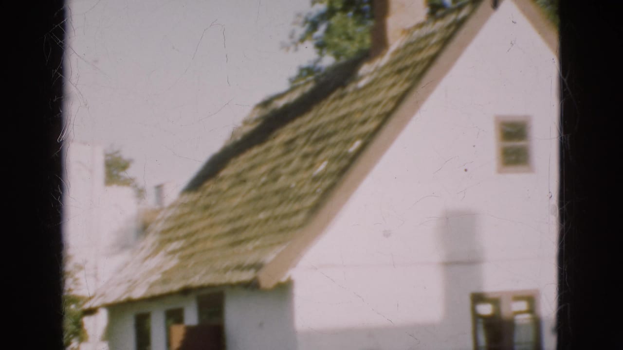 1975 Denmark 8mm frame showing a white building with a brown thatched roof, small windows, trees, and a dark doorway.