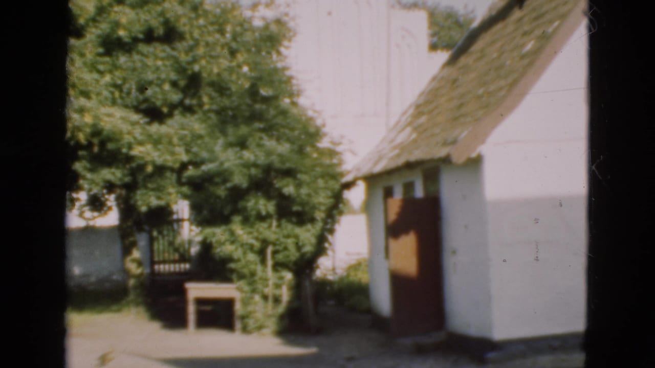 White thatched cottage beside trees with a small table in the yard.
