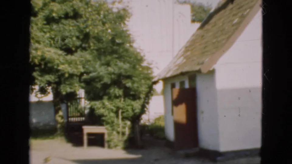1975 Denmark 8mm frame showing a white thatched cottage, trees, garden path, and small outdoor table.