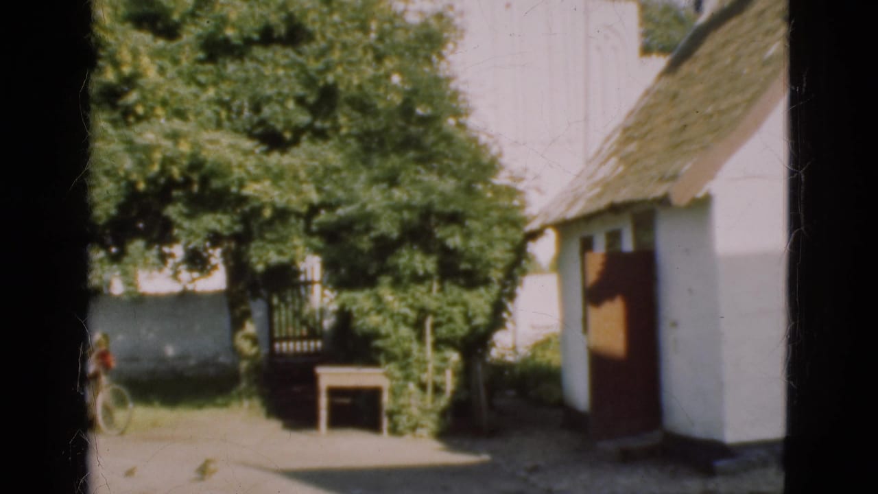 1975 Denmark 8mm frame with cottage, trees, small table, and a partly visible person beside a bicycle.