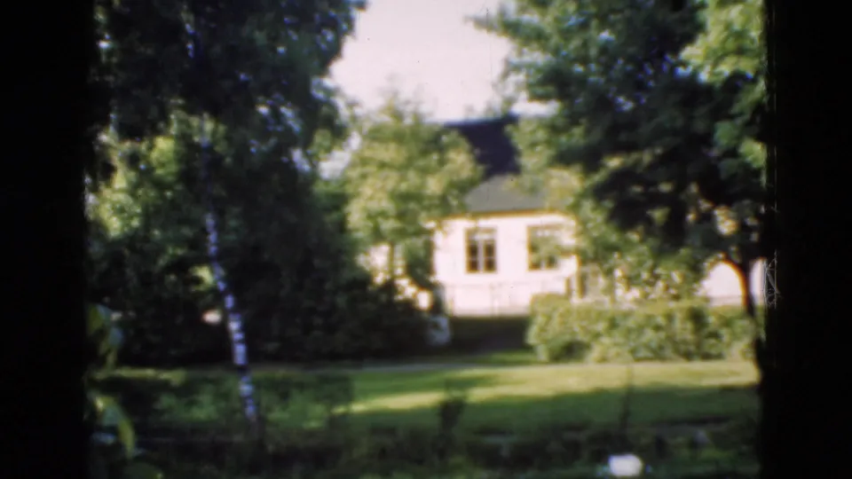 1975 Denmark 8mm frame showing a green lawn, trees, shrubs, and a light-colored house beyond the garden.