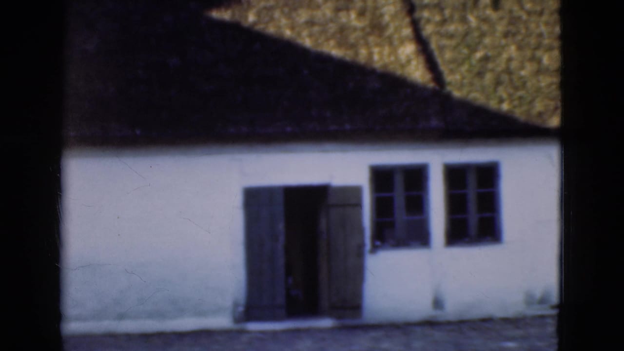 1975 Denmark frame of a whitewashed building with a thatched roof, open dark doors, and small-paned windows.