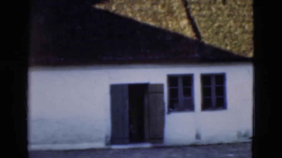 1975 Denmark frame of a whitewashed building with a thatched roof, open dark doors, and small-paned windows.