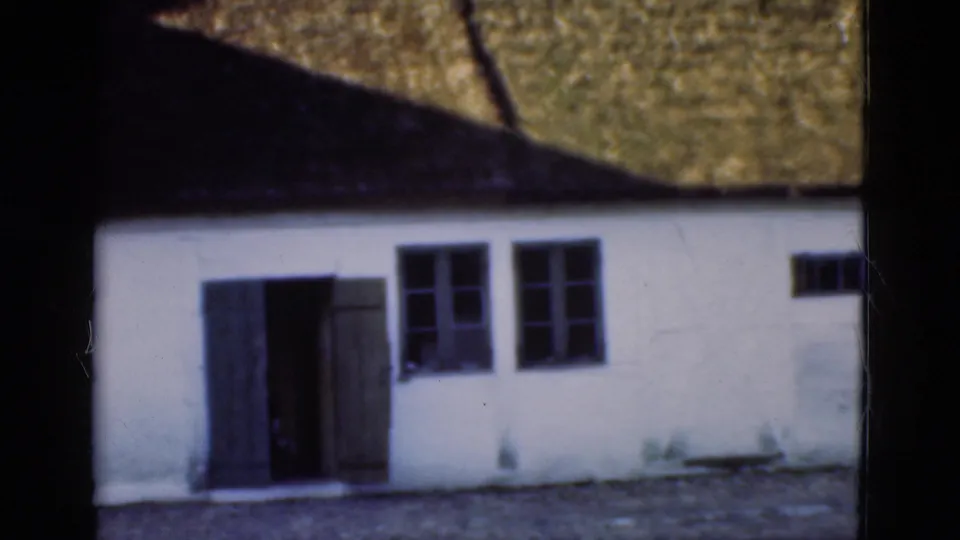 1975 Denmark home-movie frame showing the white thatched building facade with open door and dark window openings.