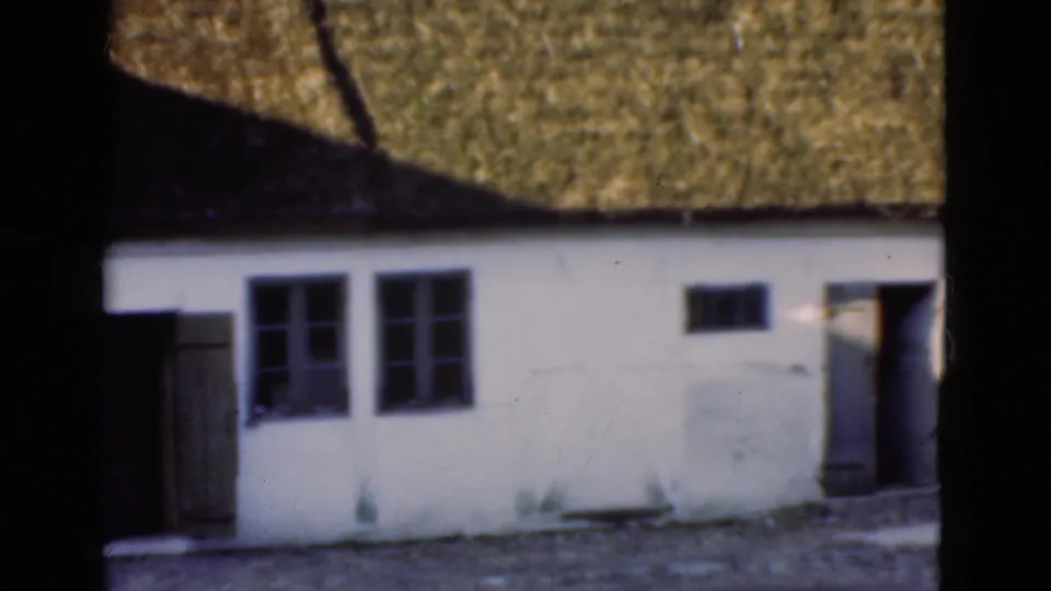 1975 Denmark frame showing a white thatched-roof facade with open doors, small windows, and a rough foreground.