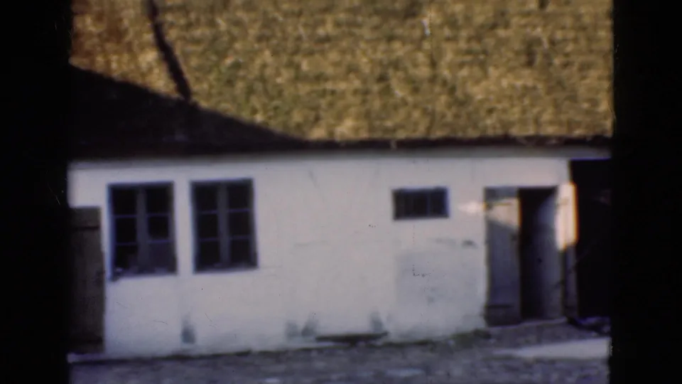 1975 Denmark 8mm frame showing a white low building with thatched roof, dark-paned windows, and a doorway in bright sun.