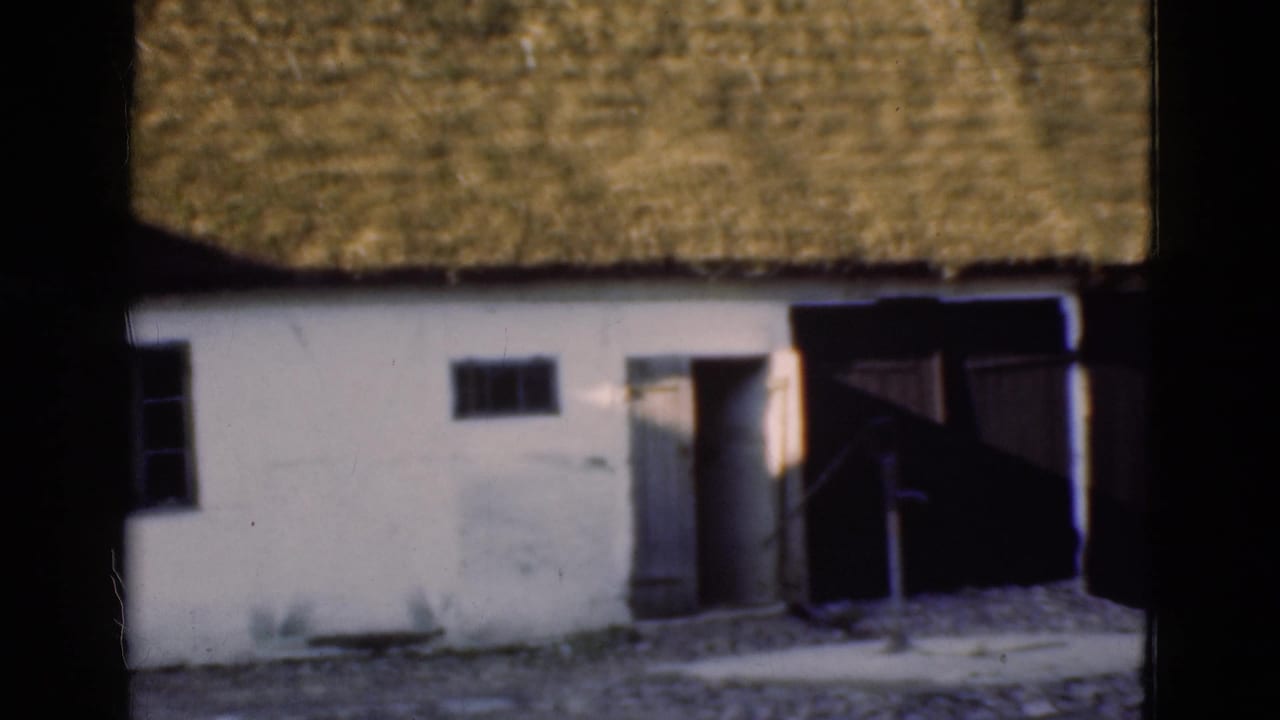 1975 Denmark 8mm frame with a white thatched-roof building, small windows, open doorway, and dark wooden doors to the side.