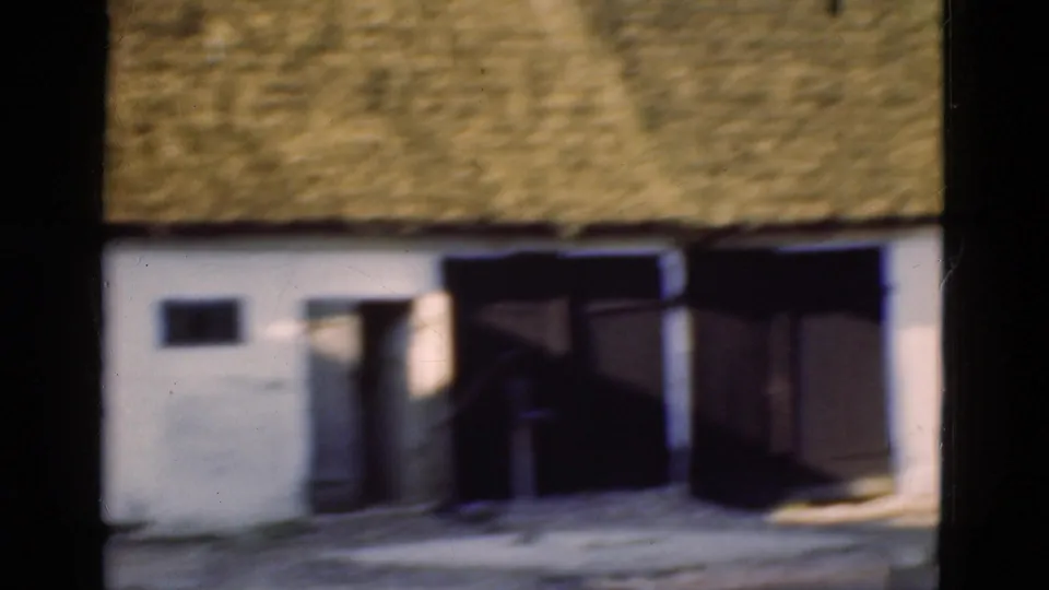 1975 Denmark 8mm frame centered on the building entrance, with white wall, thatched roof, and large dark wooden doors.