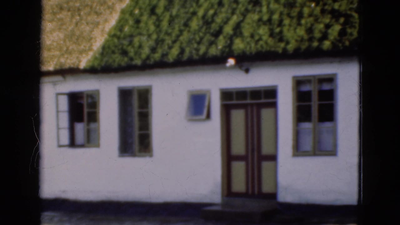 1975 Denmark 8mm frame showing the central facade of a white cottage with green thatch, a paneled double door, and windows.