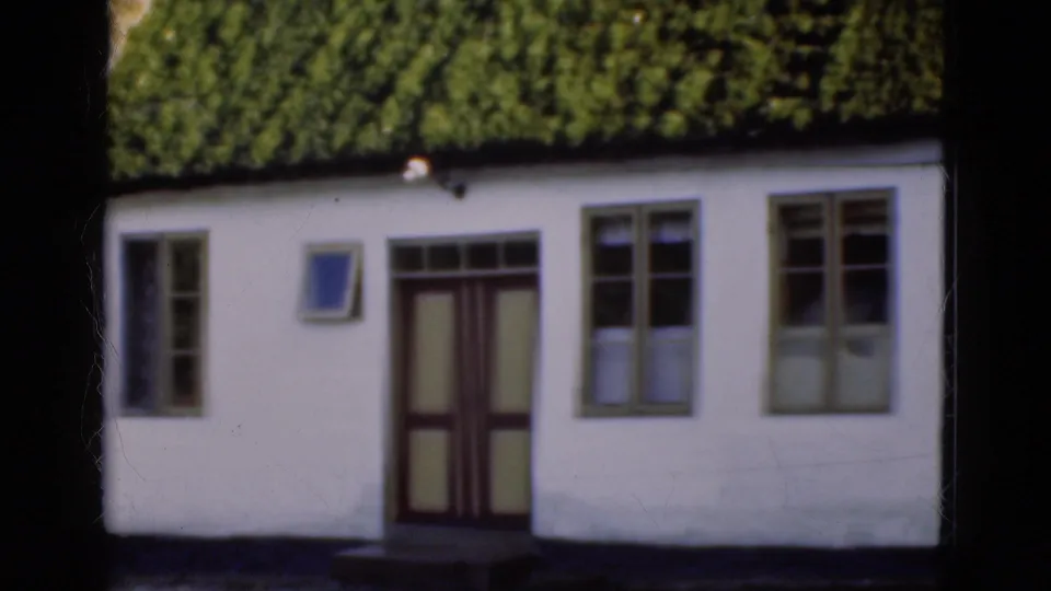 1975 Denmark 8mm frame with a closer visitor-shot view of the cottage facade, including a dark door and multi-pane windows.