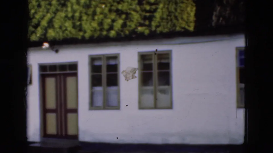 1975 Denmark 8mm frame showing the right side of the white thatched cottage with a door, paired windows, and shadowed foreground.