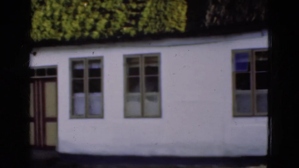 1975 Danish 8mm frame showing a white building with a dark thatched roof, multi-pane windows, and a partially seen doorway.