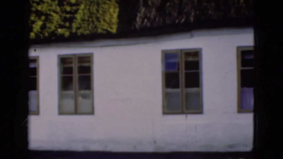 1975 Danish 8mm frame centered on a white thatched-roof exterior with repeated windows and dark window openings.