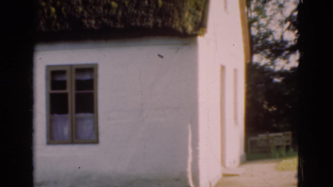 1975 Denmark 8mm frame showing a whitewashed cottage facade, small window, curtains, and thick thatched roof edge.