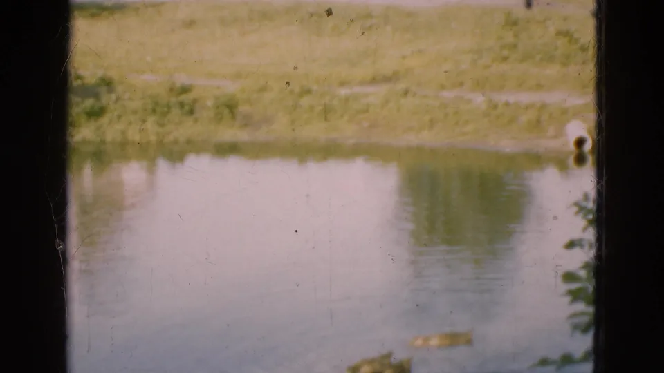 1975 Danish 8mm frame showing a calm pond with ducks and grassy banks viewed through dark window-like framing.