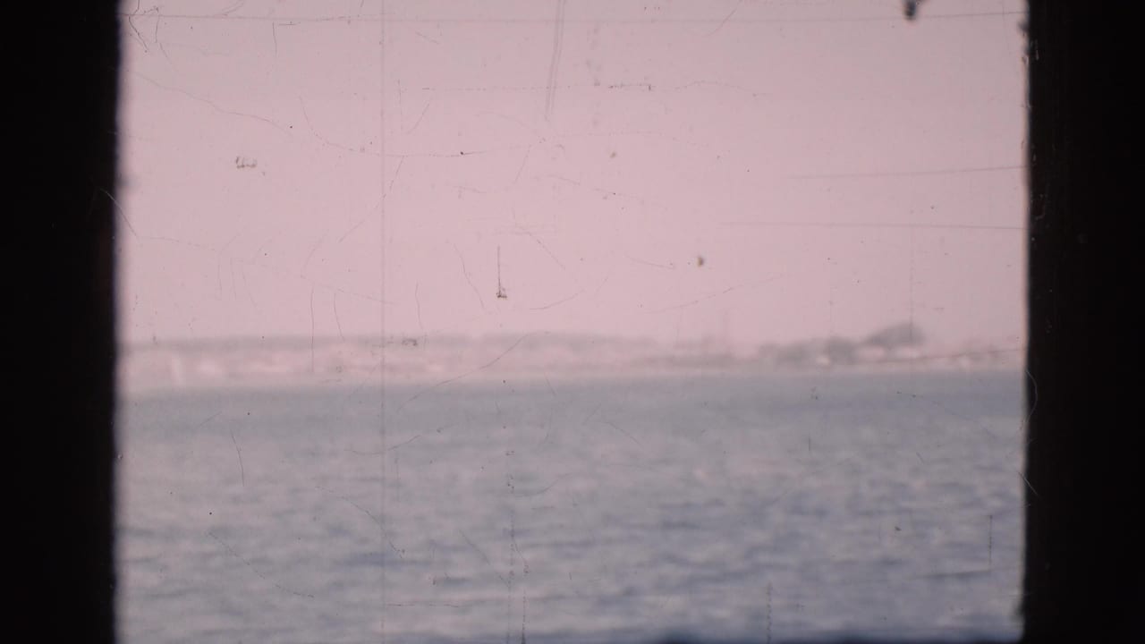 Sea and distant shoreline seen through dark boat window bars.