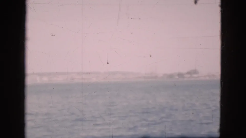 1975 Denmark 8mm view of sea and hazy shoreline framed by vertical boat window supports.