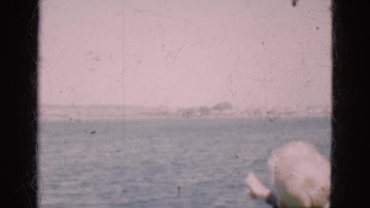 Sea view through a boat window with a person in a white cap at the edge.