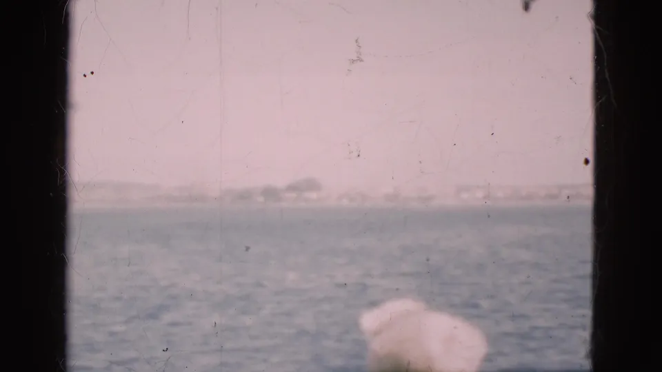 A light-haired passenger is partly visible below a hazy sea and shoreline view in 1975 Denmark home-movie footage.