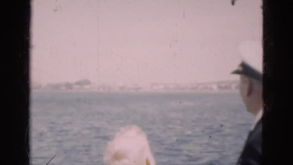 A uniformed man wearing a white captain-style hat stands by the boat window during a 1975 Denmark sea crossing.