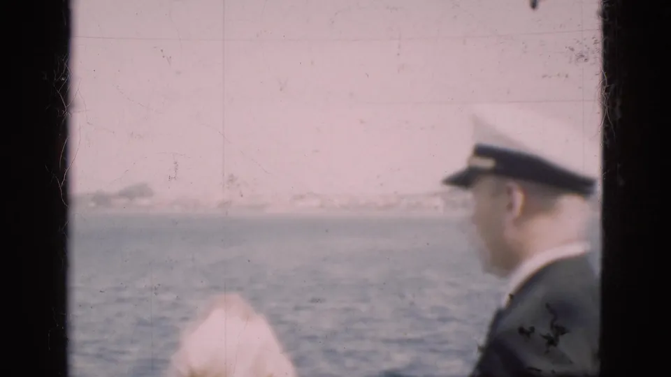 In 1975 Denmark footage, a uniformed man stands by a window facing harbor water and distant ships.