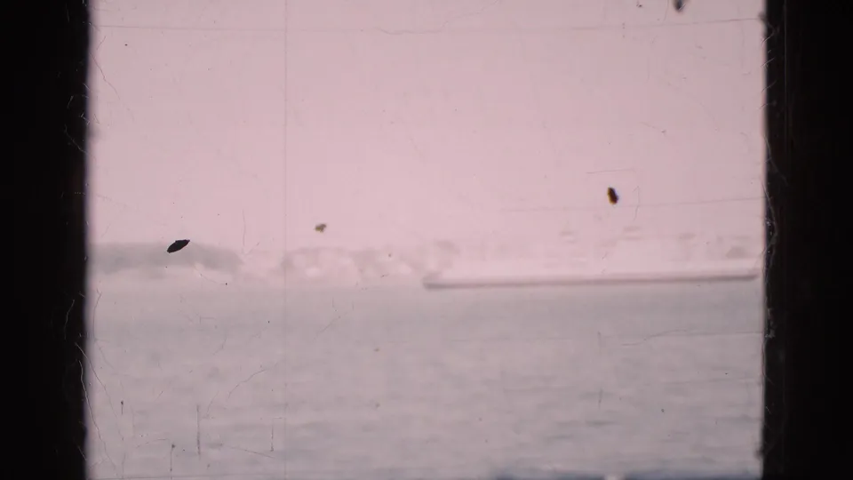 A 1975 Denmark harbor view shows calm water, a distant shoreline, and a large ship beyond dark window framing.