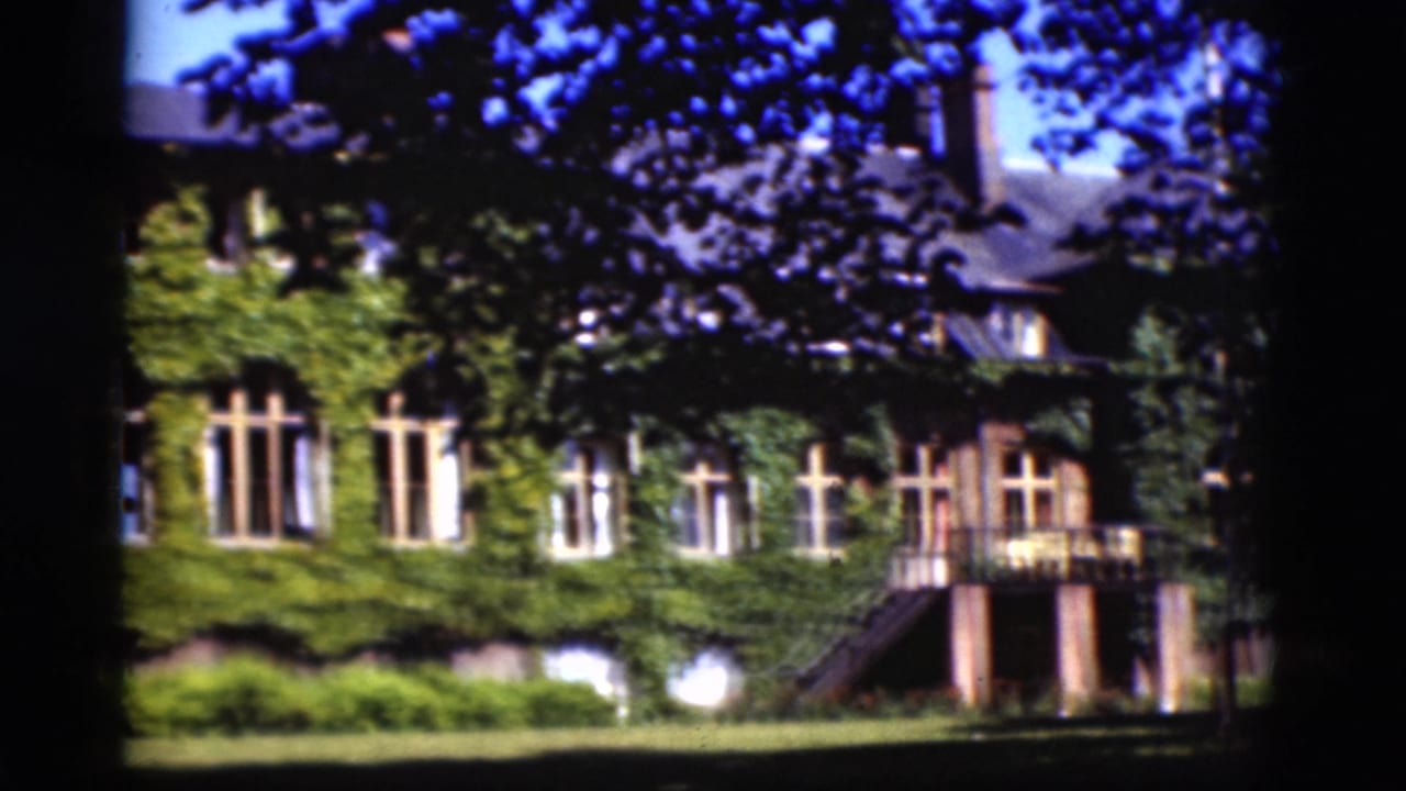 Vine-covered building with exterior stairs and balcony across a sunlit lawn.