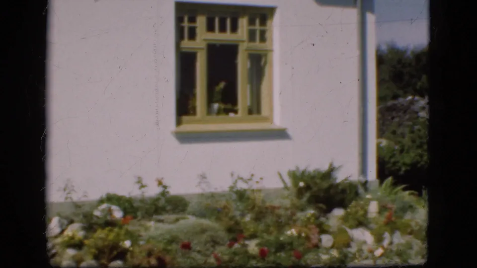 The final frame shows the garden beside a pale Danish house, with a yellow-trimmed window, shrubs, rocks, and flowers.