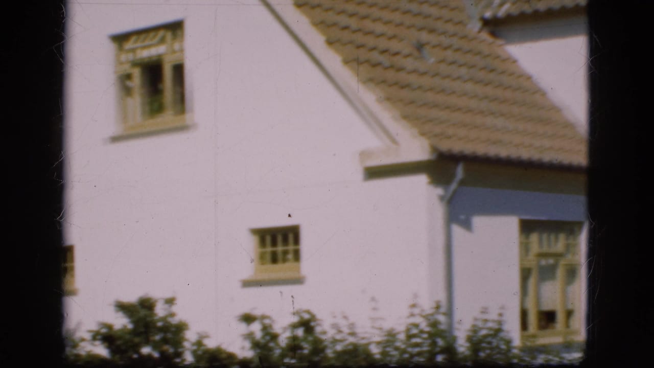 White house exterior with tiled roof, windows, grass, and shrubs in soft 8mm footage.