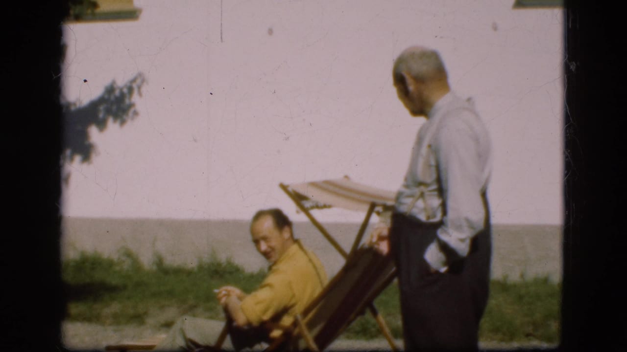 1975 Denmark 8mm frame with one man in a yellow shirt seated in a folding deck chair while another man stands beside him.