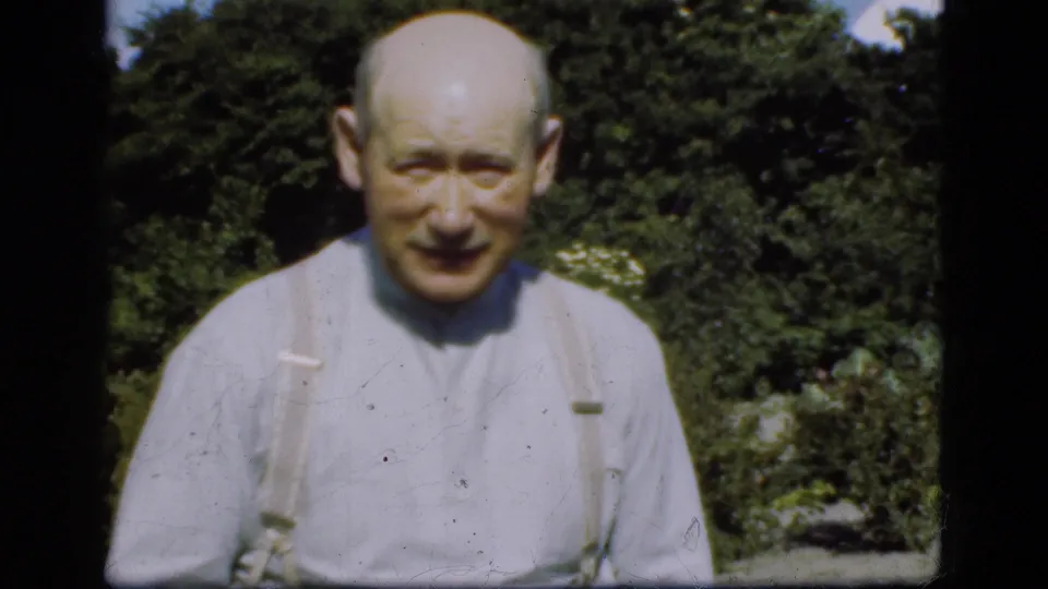 In 1975 Denmark home-movie footage, an older balding man in a light shirt and suspenders faces the camera in a garden.