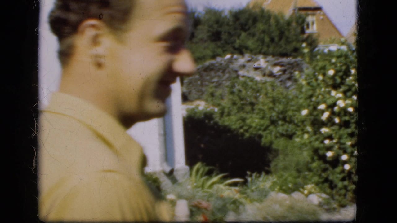 Younger man in a yellow collared shirt smiles in profile beside a garden wall.