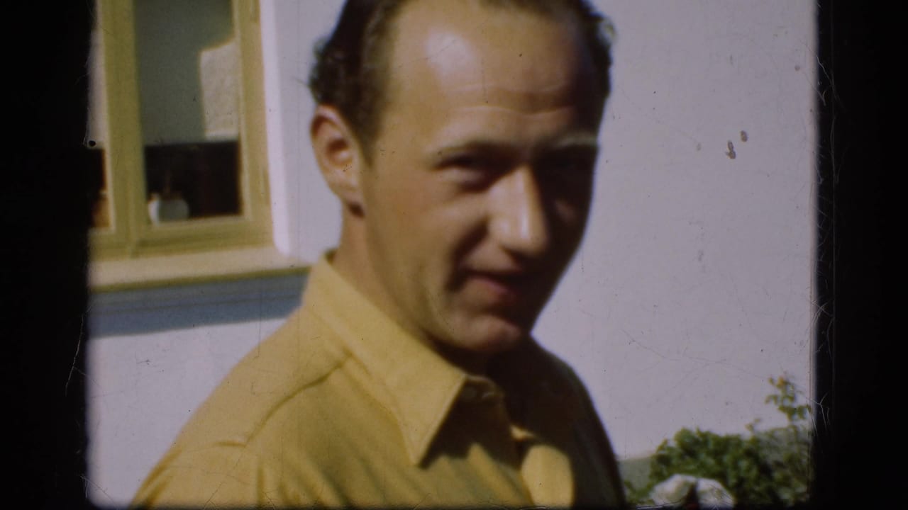 Man in a yellow shirt stands close to the camera outside a house.