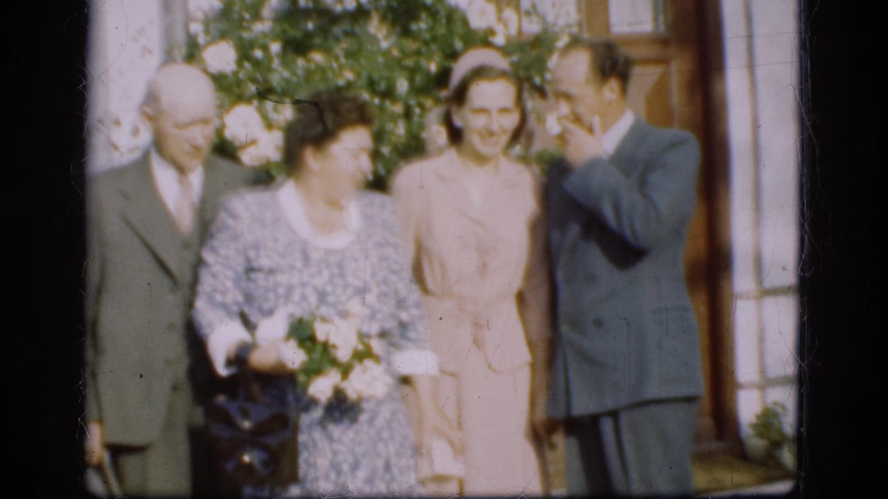 Four adults in formal clothing stand outside a building, with one woman holding flowers.