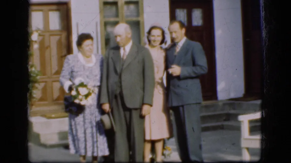 1975 Denmark frame showing four adults in formal dress outside a building, arranged as if posing for a home-movie camera.